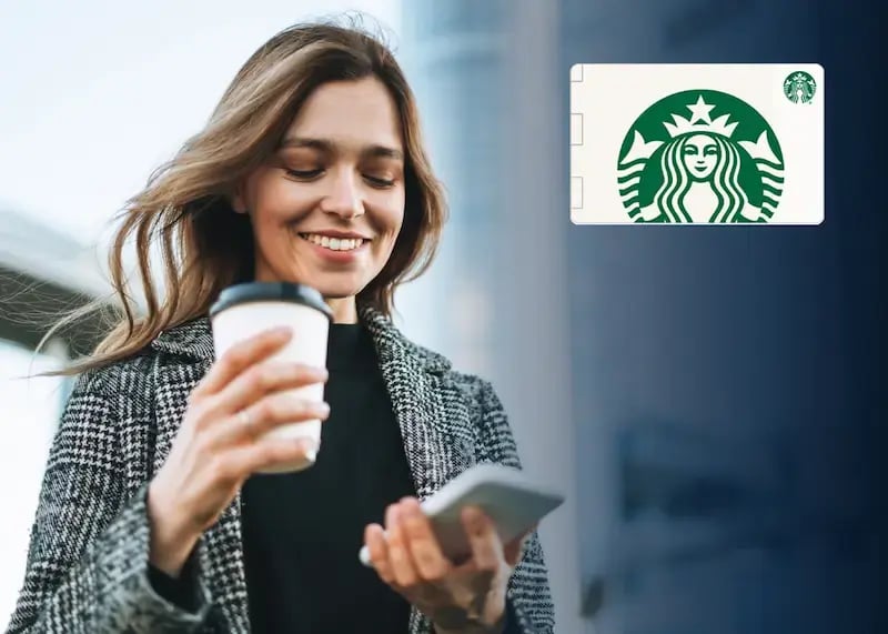 Woman drinking a coffee and looking at a gift card on her phone.