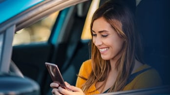 woman sitting in parked car using his cell phone to receive a digital gas gift card