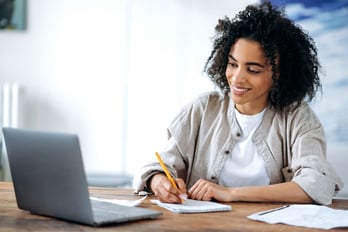 woman taking notes while watching an online lesson on her laptop