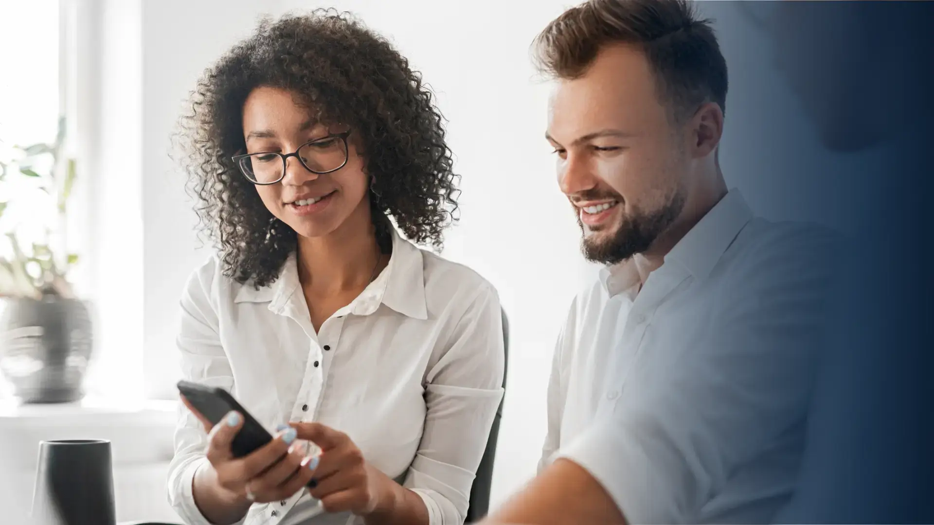 female employee showing her colleague a digital reward received on her cell phone